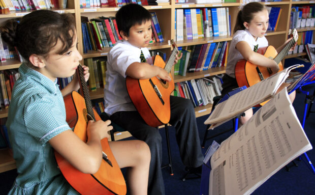 Children playing guitar in music lesson.