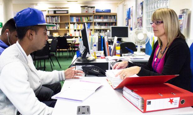 A young person speaks to a woman in a library.