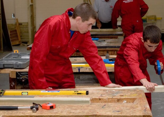 Two apprentices concentrate on sawing a piece of wood