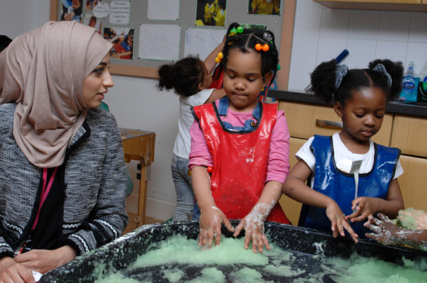 Children doing messy play while an early years staff member looks on.