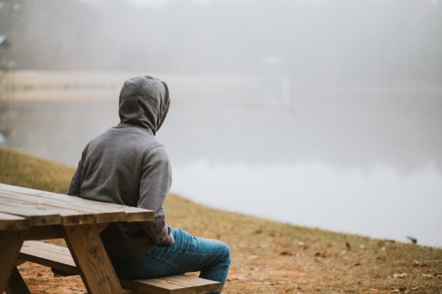 Young person in a hoodie sitting alone on a bench.