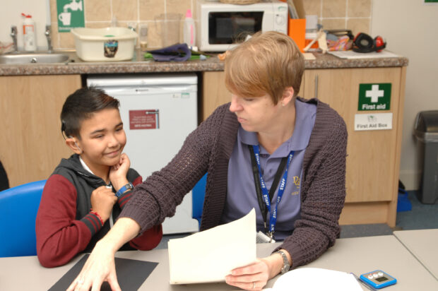 Teacher helping a pupil as they sit in a kitchen area. 