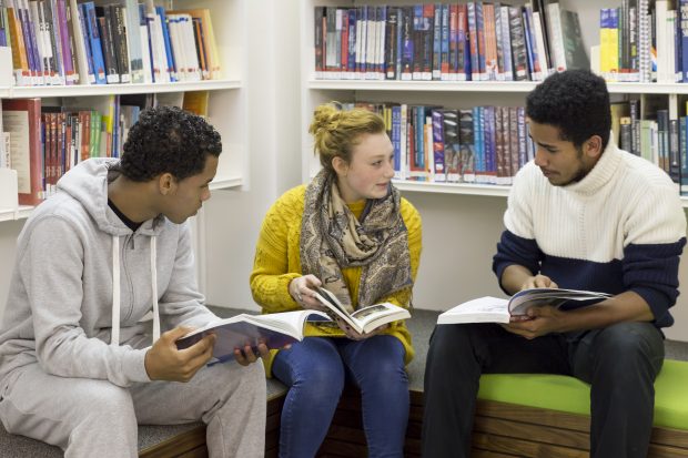 Young people in a library discussing their books. 