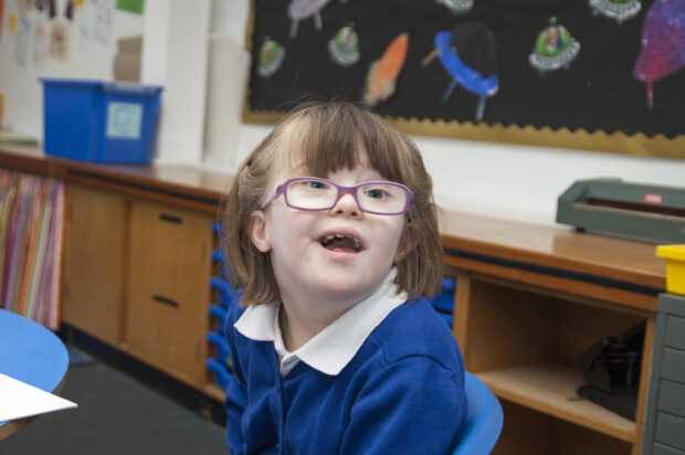 A little girl in her uniform in a special school smiling at the camera.