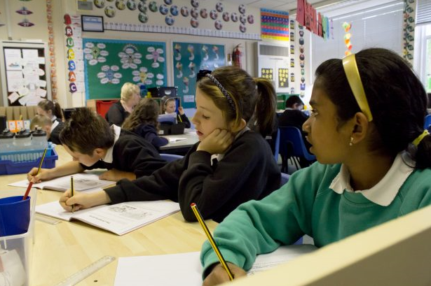 Children sat in a classroom writing in workbooks.