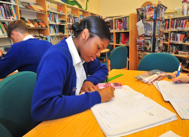 a girl at secondary school sits at a desk, writing in her book