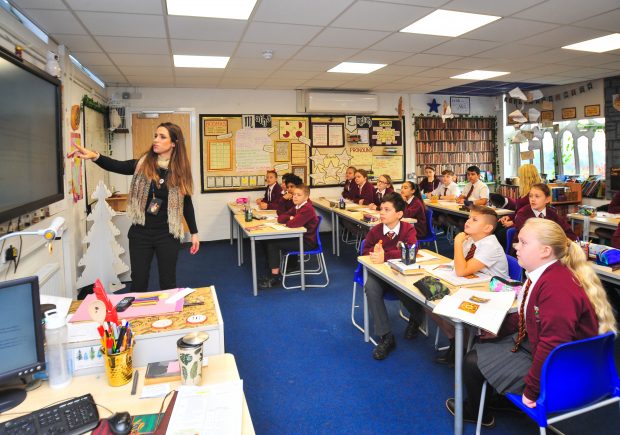 Picture of primary school pupils sat in class, with the teacher at the front of the class, using the board