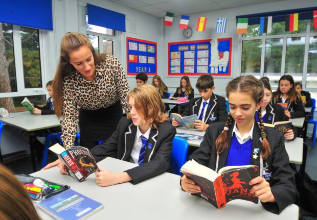 Secondary school pupils reading in class, with one pupil discussing his book with the teacher.