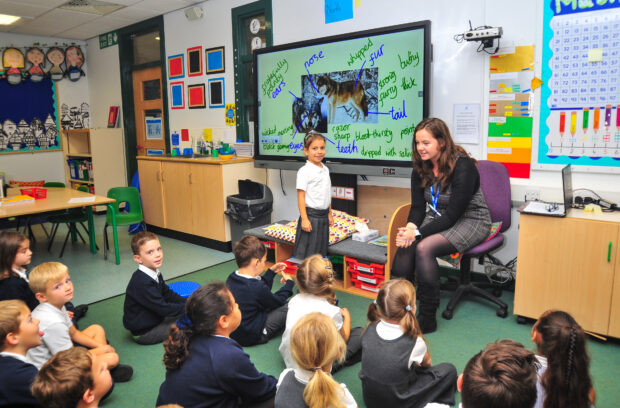 Children sat facing forward in a classroom listening to the teacher