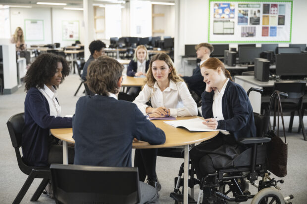 School students in uniforms sitting around a table discussing subjects and taking notes.